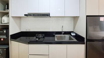 Una cocina compacta con armarios blancos, encimera negra, pileta de acero inoxidable y horno empotrado.
