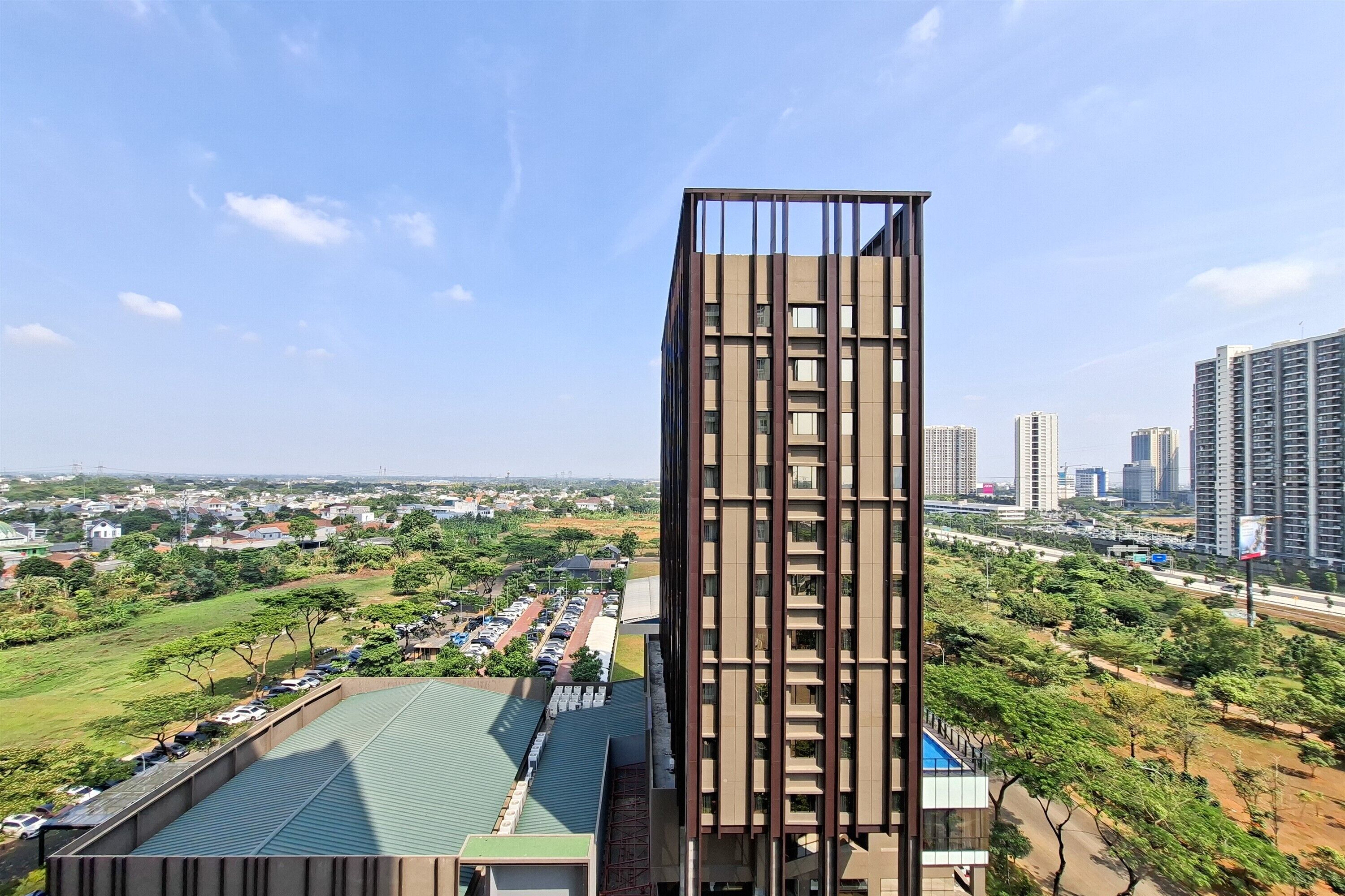 A modern high-rise building with a unique facade, surrounded by a green landscape and other high-rise buildings in the background.