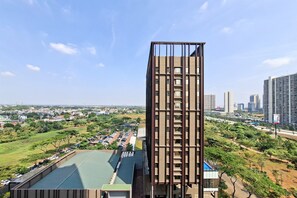 Um edifício moderno com fachada singular, cercado por paisagem verde e outros edifícios altos ao fundo.