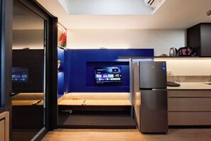 Une cuisine moderne équipée d’un téléviseur encastré, d’un réfrigérateur et d’un banc en bois.