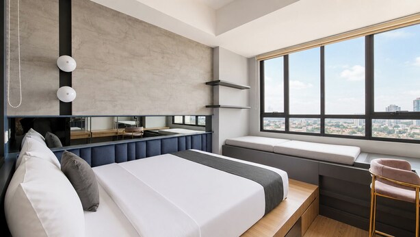 Une chambre d’hôtel moderne dotée d’un grand lit, d’un coin salon, d’une coiffeuse et d’une grande fenêtre donnant sur la ville.