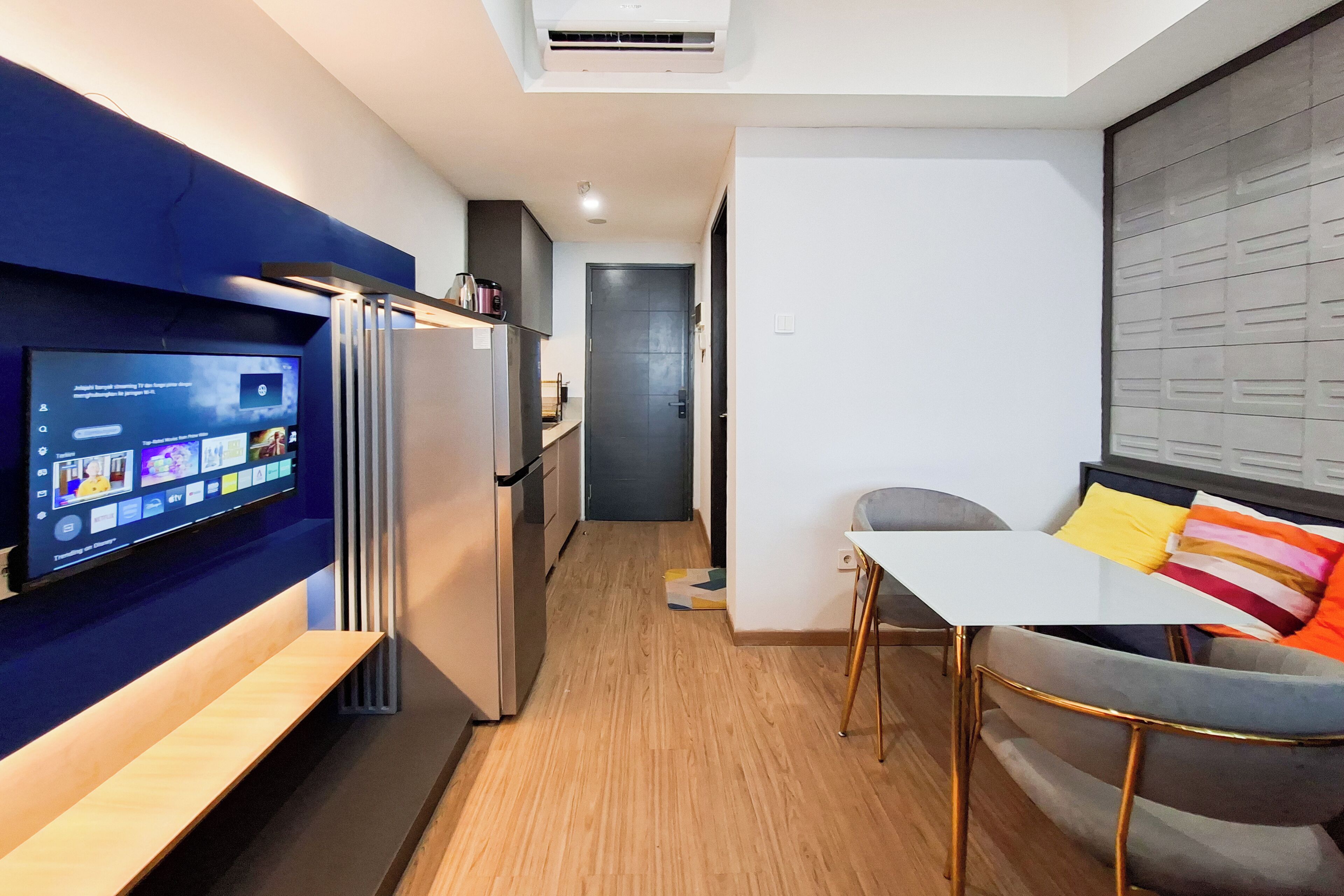 Un espacio habitable compacto con kitchenette, zona de comedor con mesa y sillas, y televisor montado en la pared.