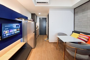 Ein kompakter Wohnraum mit Küchenzeile, einem Essbereich mit Tisch und Stühlen sowie einem an der Wand befestigten Fernseher.