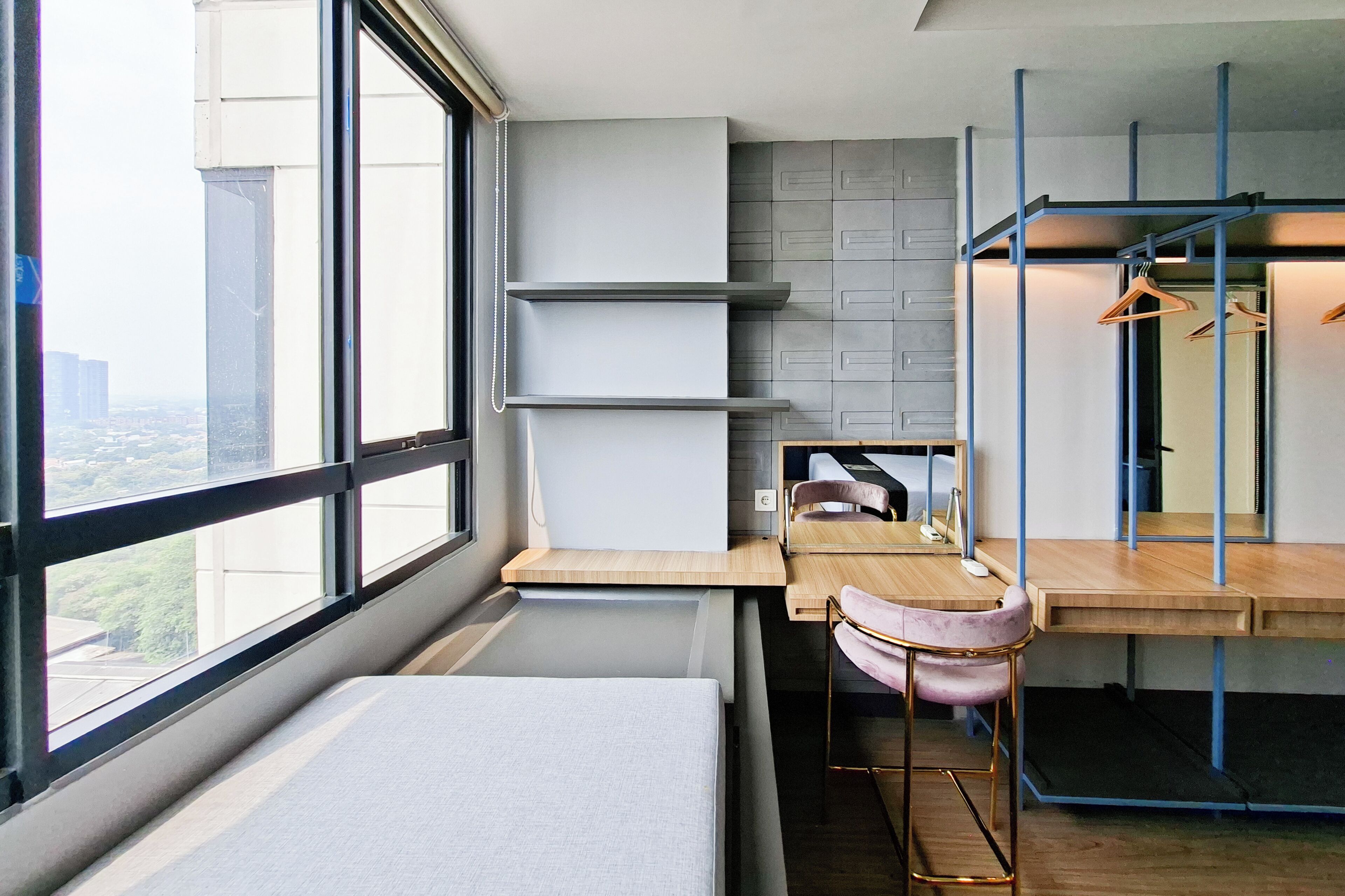 Una habitación de hotel moderna con un ventanal grande, una cama, un escritorio con una silla y un armario con ropa colgada.