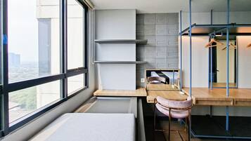 Una habitación de hotel moderna con un ventanal grande, una cama, un escritorio con una silla y un armario con ropa colgada.