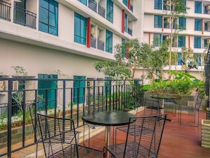 A courtyard with outdoor seating, surrounded by a metal fence, and a building with multiple balconies in the background. - Nice And Strategic Studio Room At Apartment Lrt City Bekasi (Bekasi)