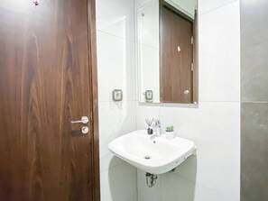 A bathroom with a wooden door, a white sink, and a mirror. - Nice And Strategic Studio Room At Apartment Lrt City Bekasi (Bekasi)