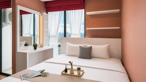 Ett modernt hotellrum med en stor säng, ett sängbord, ett fönster med gardiner och utsikt över staden.