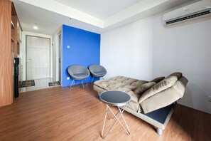 Ein kompakter Wohnbereich mit Schlafsofa, zwei Sesseln, einem kleinen runden Tisch und einer Tür zu einem weiteren Zimmer.