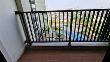 A balcony with a black metal railing overlooking a swimming pool area with a view of residential buildings.