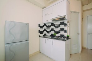 A compact kitchen with a refrigerator, a stove, and a microwave. - Cozy Minimalist 1Br At Apartment Green Pramuka City (Jakarta)