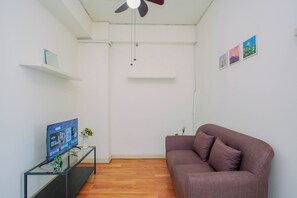 Een woonkamer met een bruine bank, een televisie op een meubelstuk, een plafondventilator en een kleine tafel met een vaas.