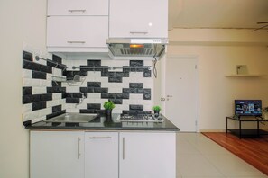 A modern kitchen with a black and white tiled backsplash, a stainless steel sink, and a gas stove. - Cozy Minimalist 1Br At Apartment Green Pramuka City (Jakarta)