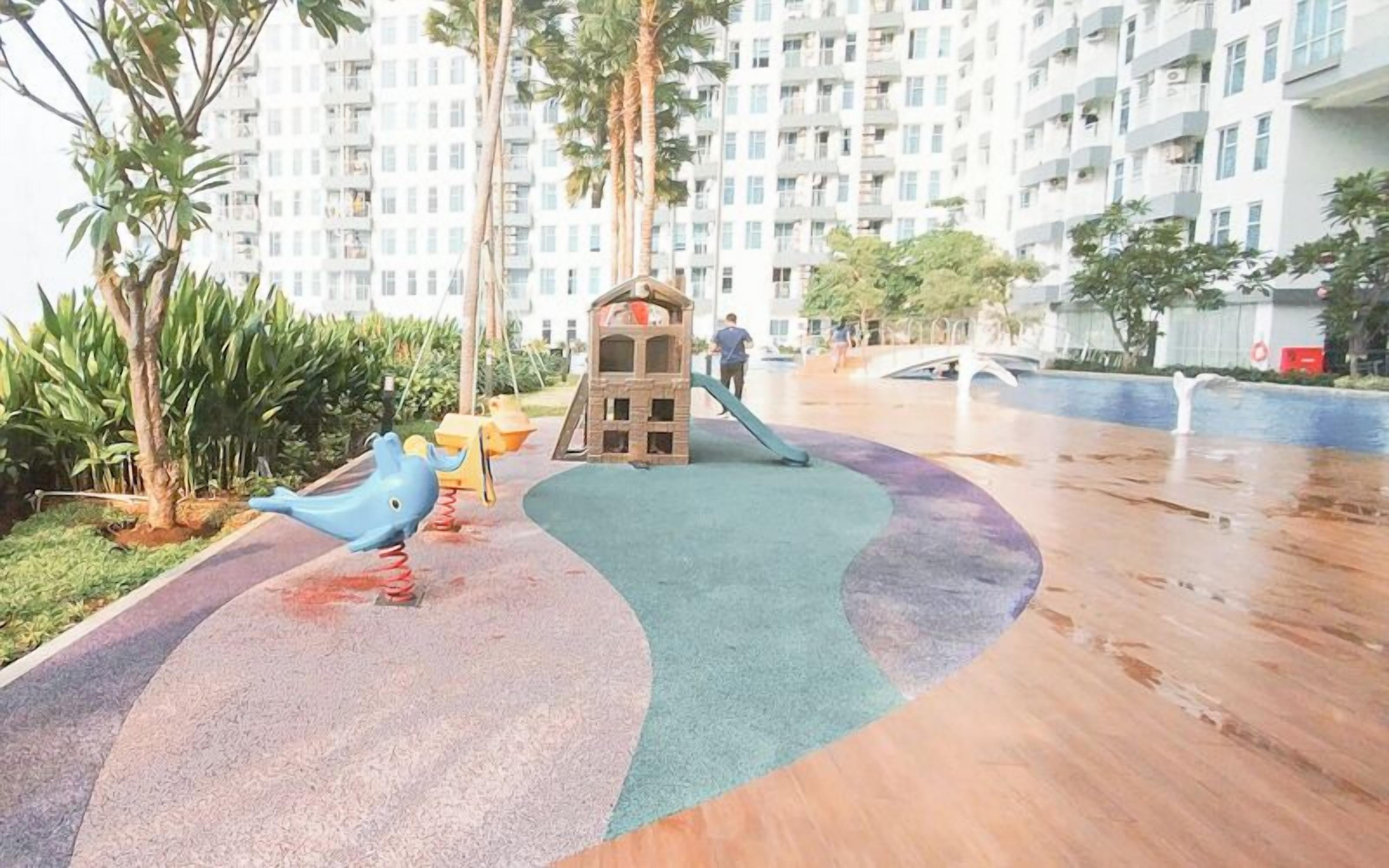 Un parque infantil con tobogán y estructuras para escalar, rodeado de palmeras y un edificio residencial al fondo.