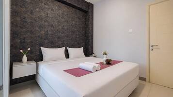 A modern hotel room with a large bed, a dark textured wall, a white door, and a small bedside table with a vase of flowers.