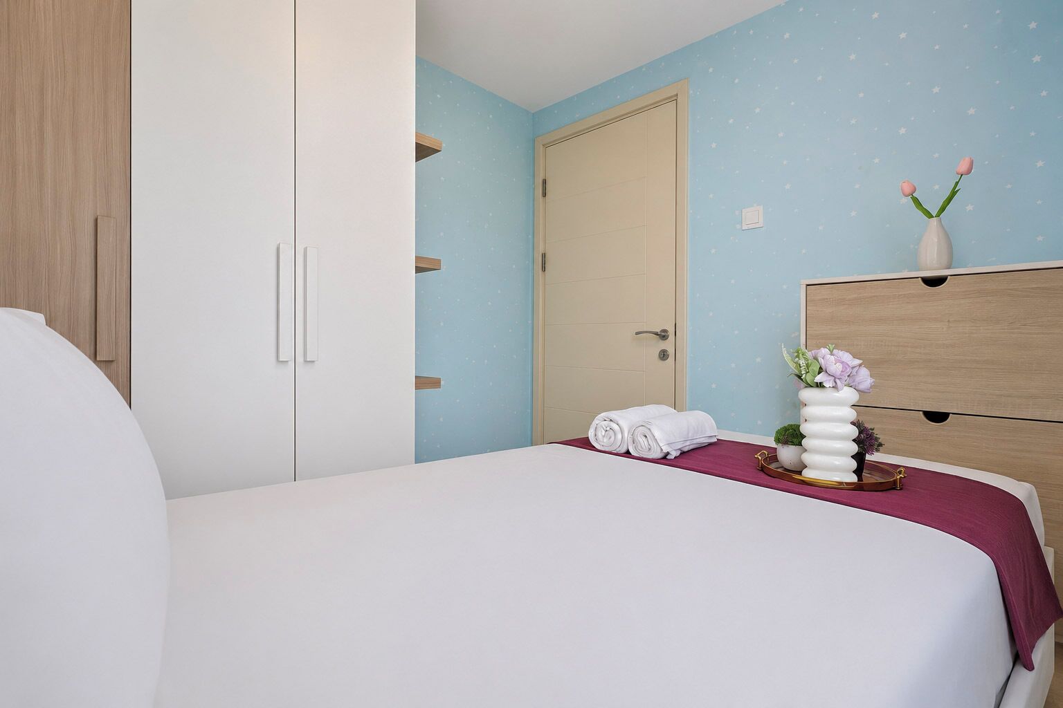 Un dormitorio con cama, armario, cómoda y mesita de noche con un florero.