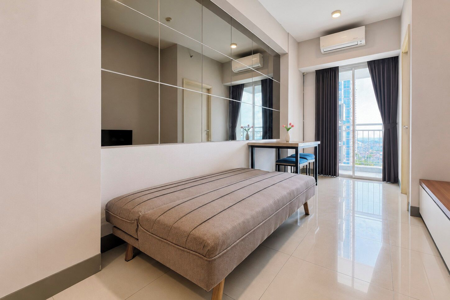 Un dormitorio moderno con una cama grande, un escritorio y vistas de la ciudad a través de un ventanal.