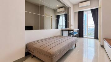 Un dormitorio moderno con una cama grande, un escritorio y vistas de la ciudad a través de un ventanal.