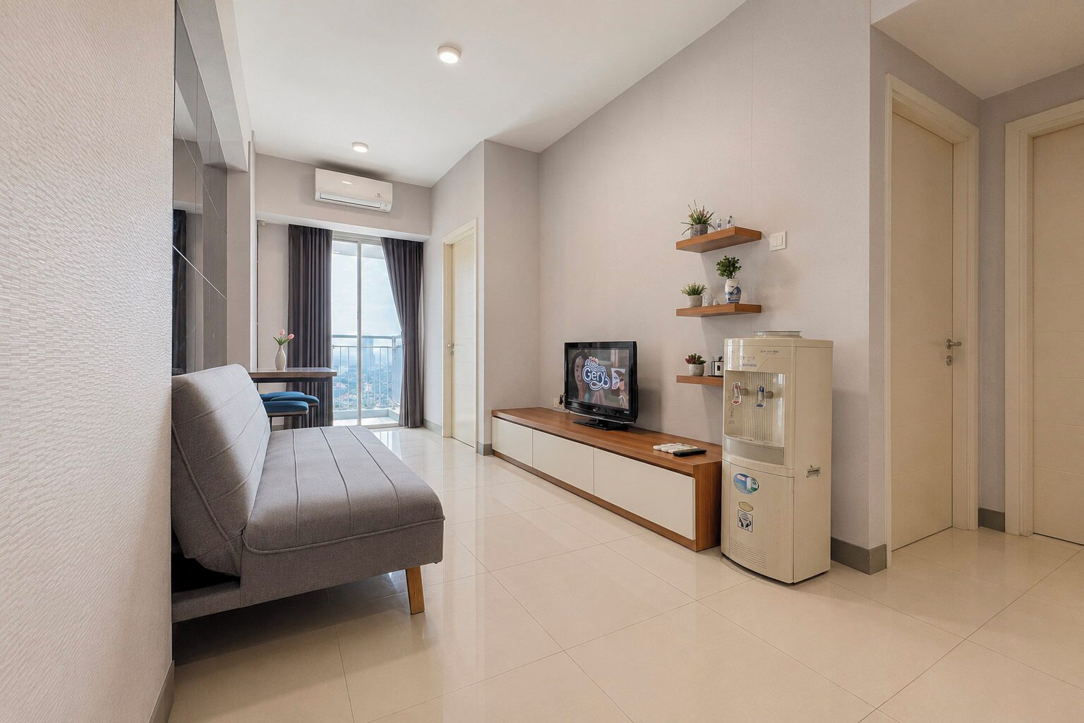 Una sala de estar moderna con un sofá, un televisor, un refrigerador pequeño y un balcón con cortinas.
