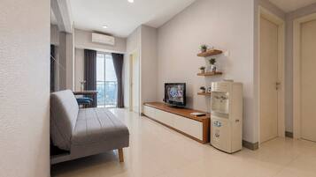 Una sala de estar moderna con un sofá, un televisor, un refrigerador pequeño y un balcón con cortinas.