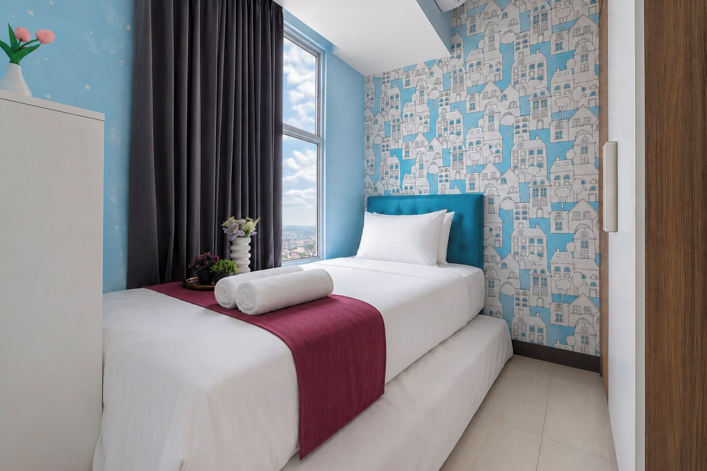 Une chambre d’hôtel avec un lit, une fenêtre, un rideau, un vase de fleurs et un mur orné d’un motif.