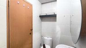 A small bathroom with a toilet, a sink, and a wooden door. - Sleek Modern Studio At Apartment Pinewood (Sumedang)