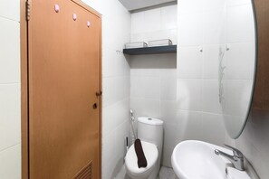 A small bathroom with a toilet, a sink, and a wooden door. - Sleek Modern Studio At Apartment Pinewood (Sumedang)
