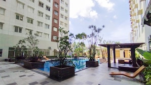 A courtyard with a swimming pool, potted plants, outdoor seating, and high-rise buildings in the background. - Sleek Modern Studio At Apartment Pinewood (Sumedang)