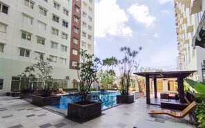 A courtyard with a swimming pool, potted plants, outdoor seating, and high-rise buildings in the background. - Sleek Modern Studio At Apartment Pinewood (Sumedang)