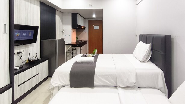 A hotel room with a bed, a TV, a kitchenette, and a door. - Sleek Modern Studio At Apartment Pinewood (Sumedang)