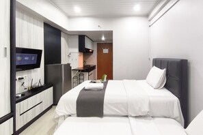 Una habitación de hotel con cama, televisor, kitchenette y una puerta.