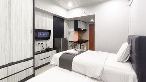 A modern hotel room with a bed, a desk, a flat-screen TV, and a kitchenette. - Sleek Modern Studio At Apartment Pinewood (Sumedang)