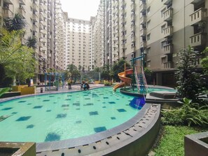 A swimming pool with a slide, surrounded by greenery and residential buildings. - Warm Homey 2Br At Apartment Gateway Ahmad Yani Cicadas (Bandung)
