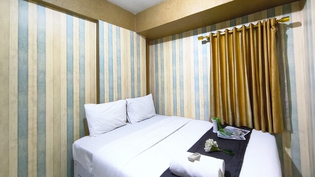 Habitación de hotel con cama, paredes a rayas, una ventana con cortinas y una mesita con un control remoto y una flor.