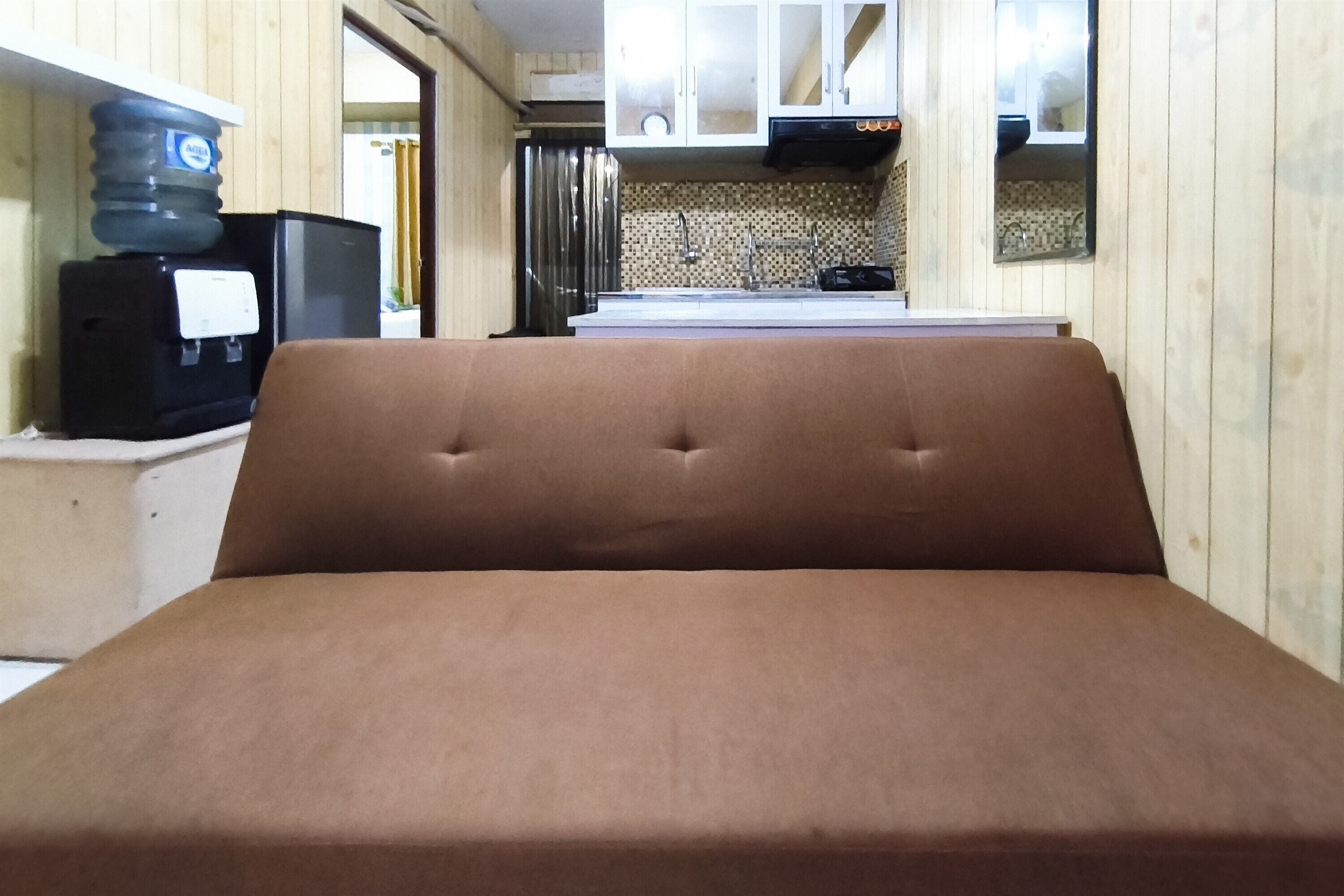 A single bed in a room with a kitchenette in the background.
