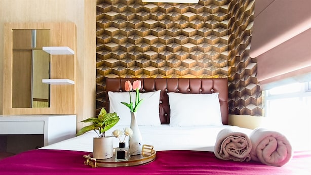 A hotel room with a bed, a bedside table, a mirror, and a patterned wall. - Serene And Warm 1Br At Apartment Tamansari Prospero Sidoarjo (Sidoarjo)