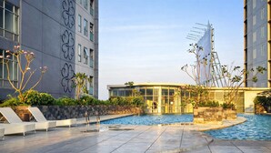 A modern building with a swimming pool, lounge chairs, and a glass-enclosed structure. - Serene And Warm 1Br At Apartment Tamansari Prospero Sidoarjo (Sidoarjo)