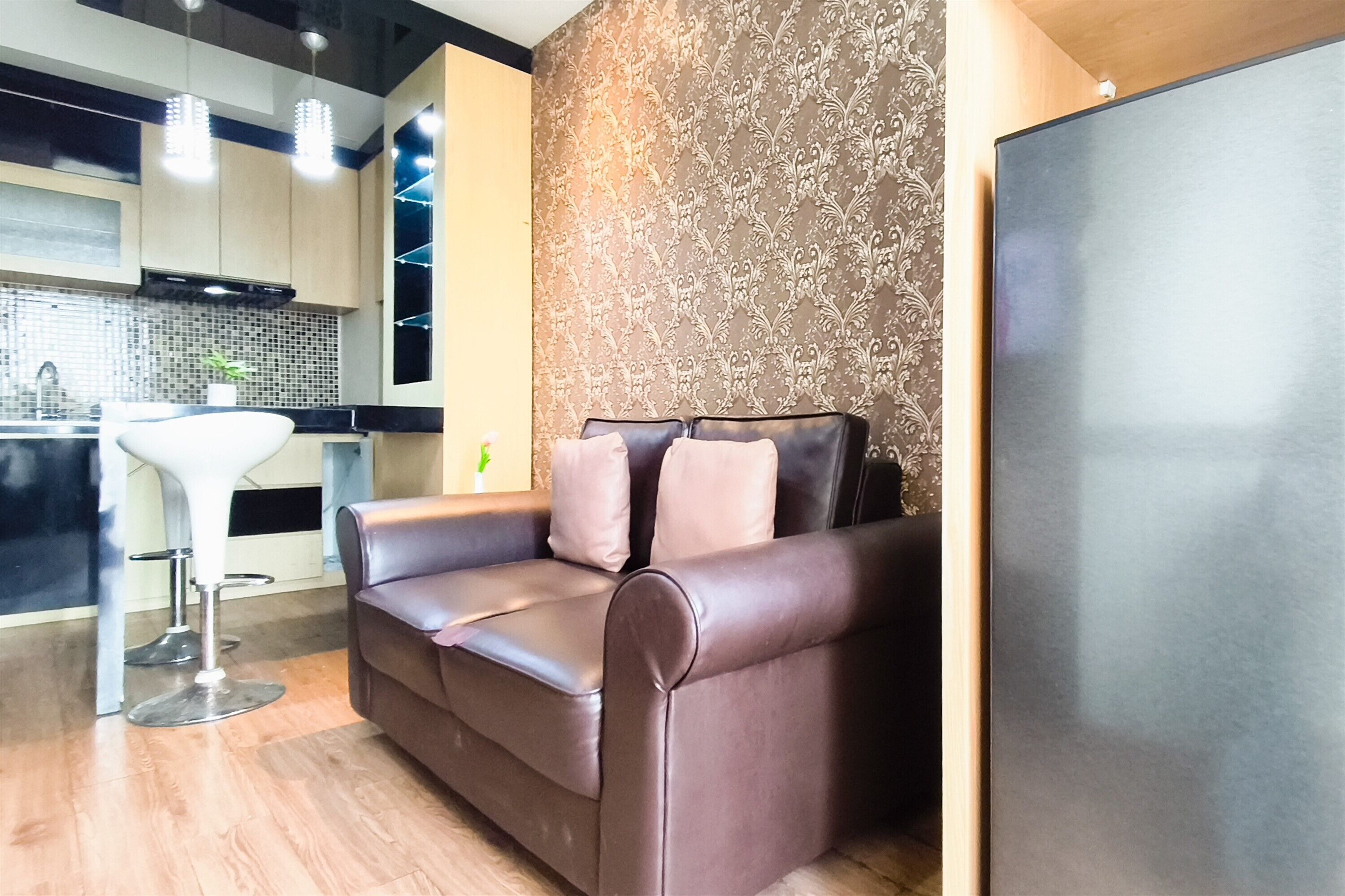 A modern living area with a sofa, a bar stool, and a kitchen in the background.