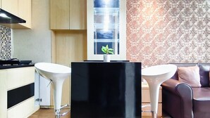 A modern kitchen with two white bar stools, a black central table, and a patterned wallpaper wall. - Serene And Warm 1Br At Apartment Tamansari Prospero Sidoarjo (Sidoarjo)