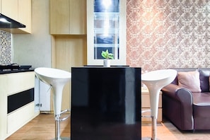 Ett modernt kök med två vita barstolar, ett svart bord i mitten och en vägg med mönstrat tapet.