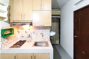 A compact kitchen with a gas stove, a sink, and wooden cabinets. - Comfortable 2Br At Apartment Gateway Ahmad Yani Cicadas (Bandung)