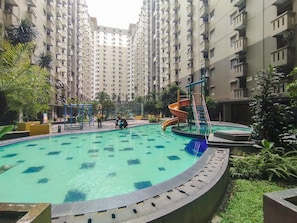 Ein Swimmingpool mit Rutsche, umgeben von Grünflächen und Wohngebäuden.
