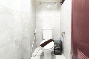 Ein kleines Badezimmer mit Fliesen, einer Toilette, einem Händetrockner und einem Mülleimer.