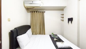 A hotel room with a bed, a bedside table, a remote control, and a window with curtains. - Comfortable 2Br At Apartment Gateway Ahmad Yani Cicadas (Bandung)