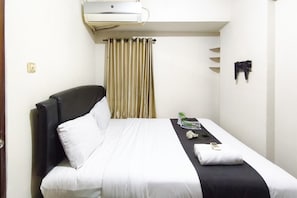 Ein Hotelzimmer mit Bett, Nachttisch, Fernbedienung und einem Fenster mit Vorhängen.