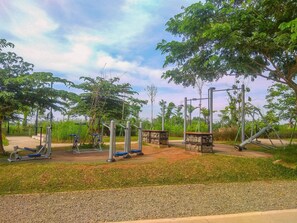 Ein Outdoor-Fitnessbereich mit Trainingsgeräten, umgeben von Bäumen und viel Grün.