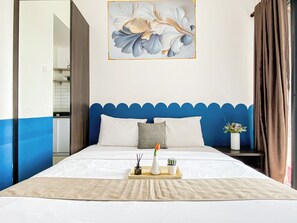 Ein Hotelzimmer mit einem Bett, einer blauen Akzentwand, einem Gemälde, einem Nachttisch und einem Fenster mit Vorhängen.