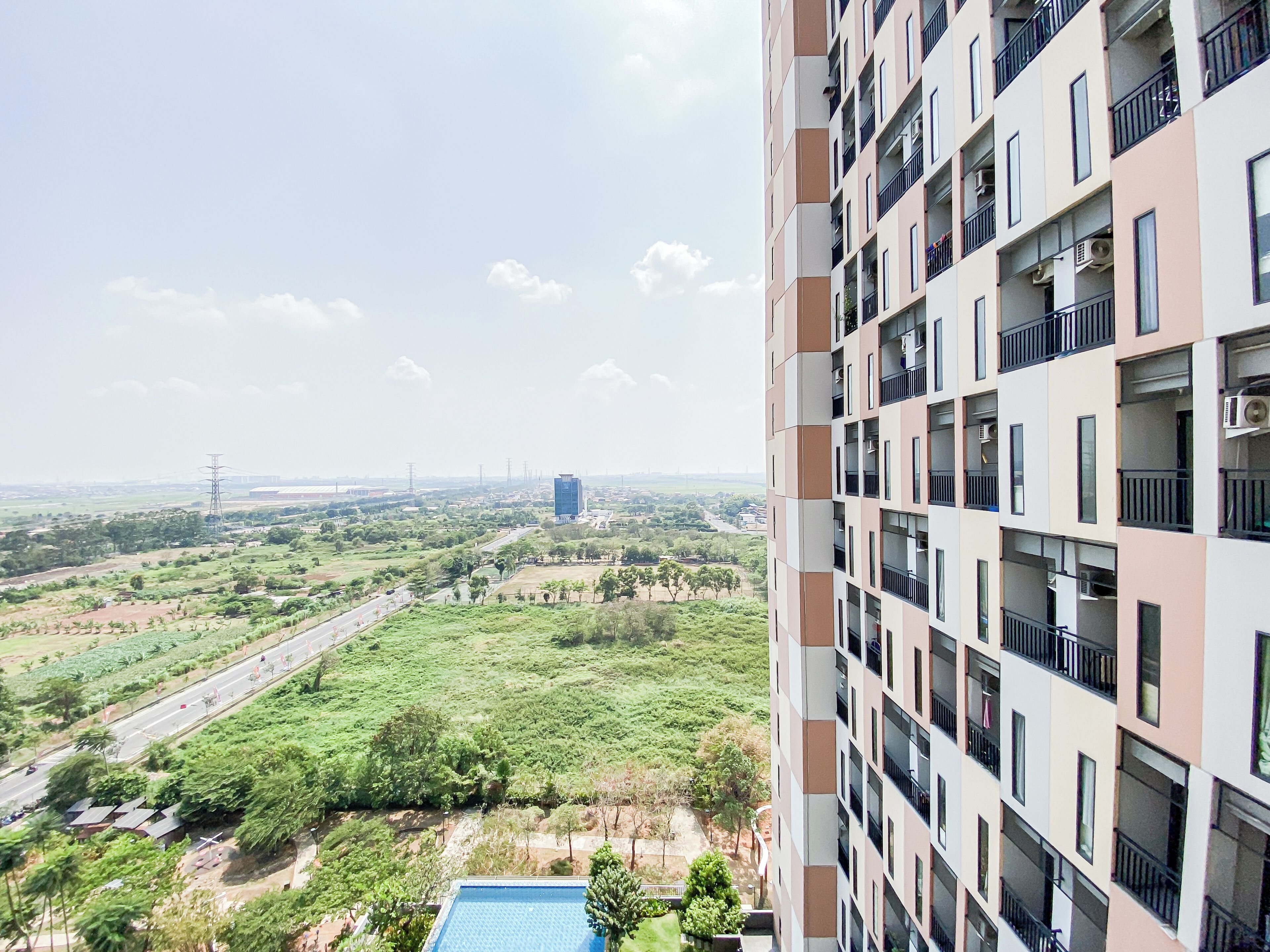 A high-rise building with multiple balconies and a view of a green landscape with trees and a road.