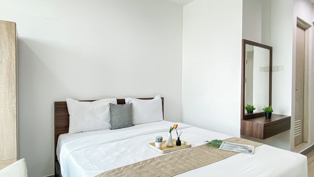 A neatly made bed with pillows, a bedside table with a tray, and a mirror. - Comfortable And Minimalist Studio Room At Apartment Grand Kamala Lagoon (Bekasi)