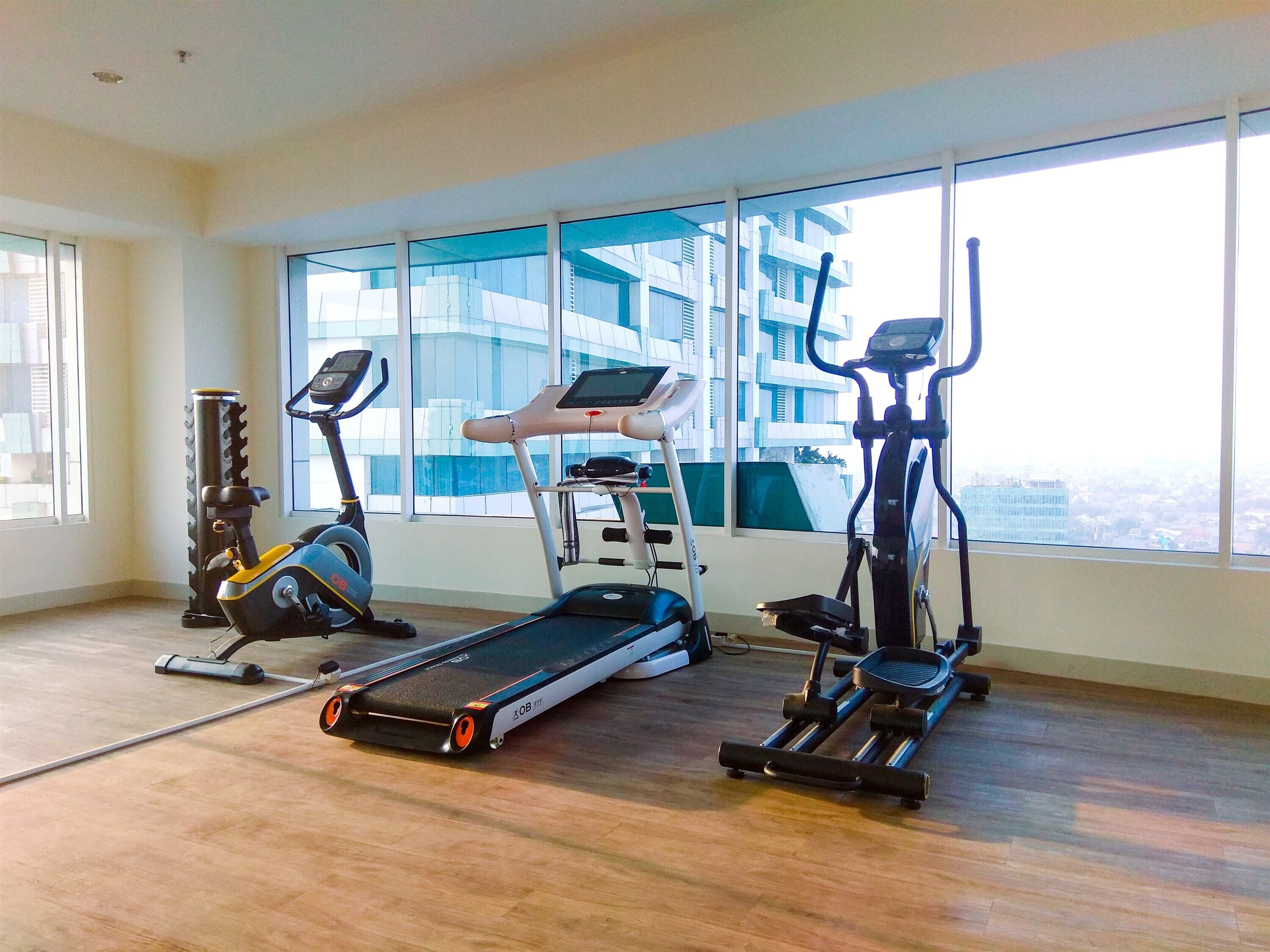 Un gimnasio con cintas de correr, elíptica y máquina de remo, amplias ventanas con vista a la ciudad.